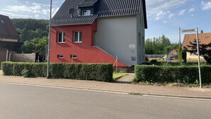 A two-story house with a red and grey facade, a tiled roof, and a satellite dish.