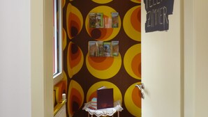 A narrow hallway with a patterned wall, a radiator, a small table with a book, and a door with a sign.