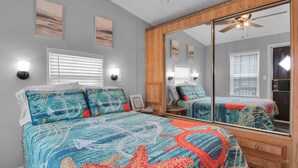 A bedroom with a large bed, a wooden wardrobe, a ceiling fan, and a large mirror.