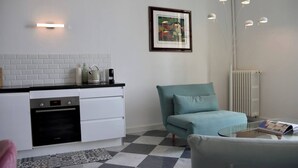 Una cocina moderna con horno Bosch, un armario blanco, un sillón verde azulado, una mesa de centro de vidrio y un cuadro en la pared.
