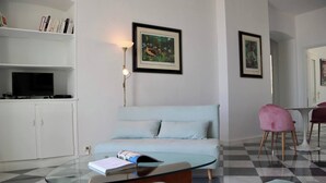 Una sala de estar con una mesa de centro de vidrio, un sofá azul claro, un mueble blanco con un televisor y una silla rosa.