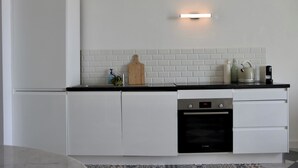 Una cocina moderna con armarios blancos, encimera negra, horno empotrado y lámpara fijada a la pared.