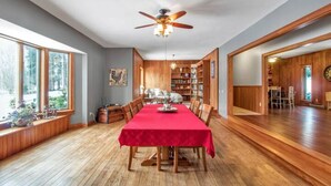 A dining room with a red tablecloth, wooden flooring, and a ceiling fan.