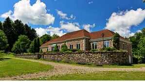 A stone building with a red roof, surrounded by a stone wall and lush greenery.