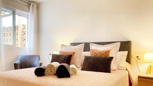 Een keurig opgemaakt bed met een geborduurd sprei, twee opgerolde handdoeken en meerdere kussens.
