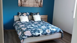 Una cama con cubrecama floral, cabecera de madera y lámpara colgante blanca.