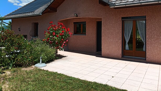 Una casa con techo de tejas, un ventanal con cortinas y un jardín con flores rojas.