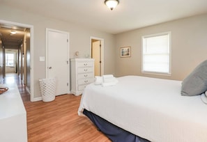 Une chambre à coucher avec un grand lit, une commode, un dressing et un couloir menant aux autres pièces.
