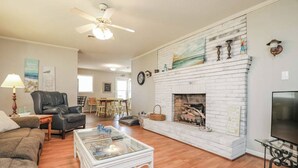 A living room with a white brick fireplace, a glass coffee table, a sofa, a leather chair, and a TV. - Sneads Ferry 4BR Waterfront Home Near Camp Lejeune (Sneads Ferry)