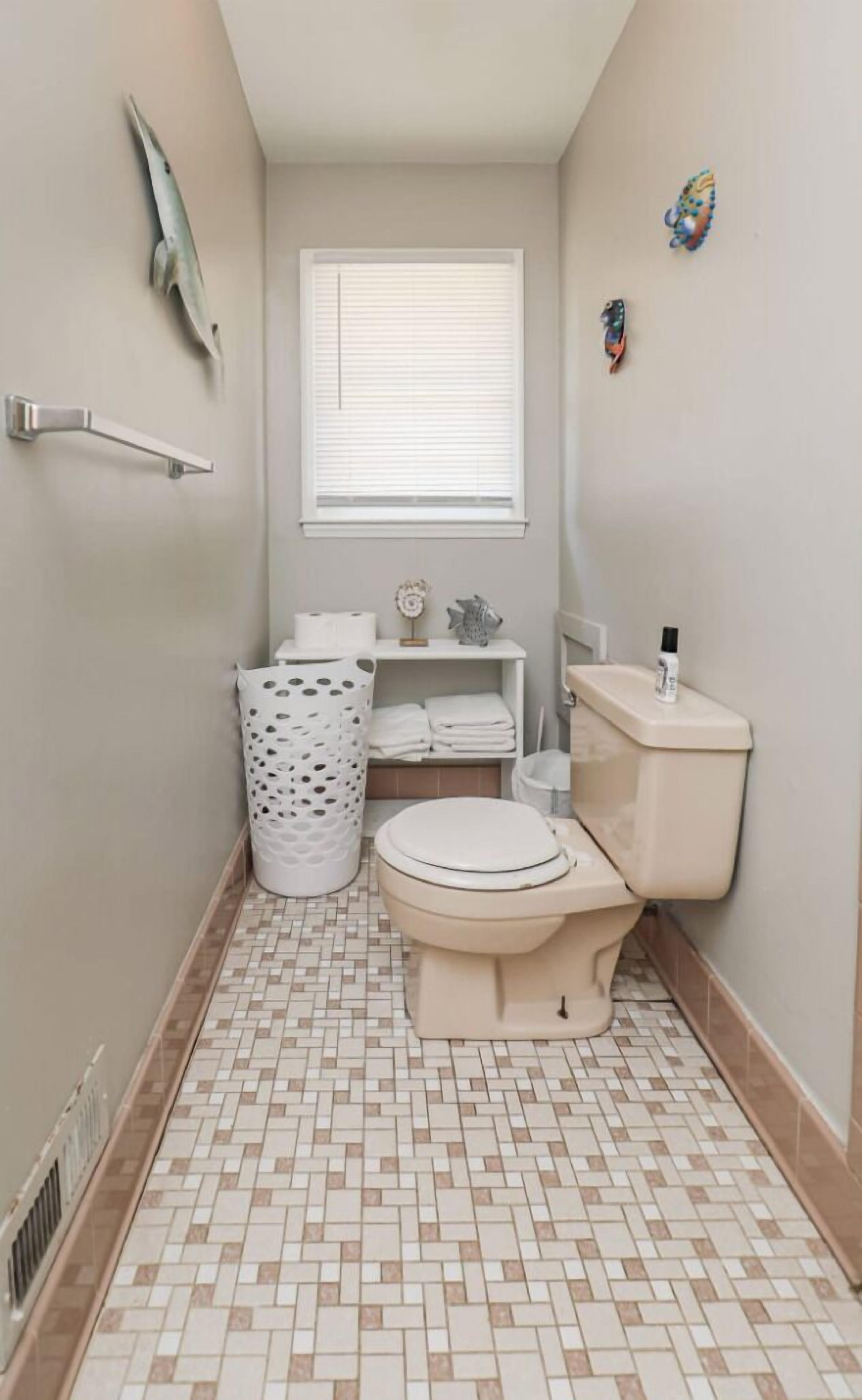 Une petite salle de bain comprenant des toilettes, un lavabo, une fenêtre et une poubelle.