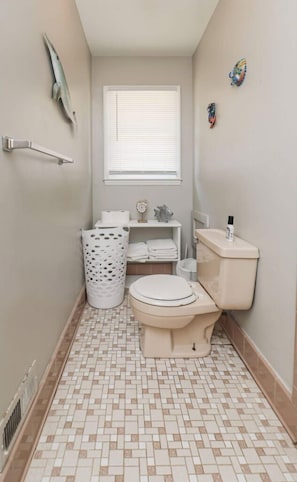 Une petite salle de bain comprenant des toilettes, un lavabo, une fenêtre et une poubelle.