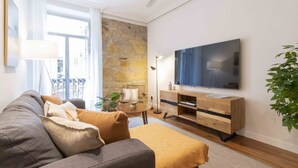 A modern living room with a grey sofa, a wooden TV stand, and a large flat-screen TV. - San Martin II | The Rentals Collection (San Sebastián)