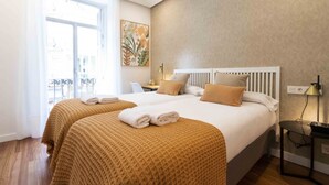 A hotel room with two beds, a large window, a balcony, and a painting on the wall. - San Martin II | The Rentals Collection (San Sebastián)