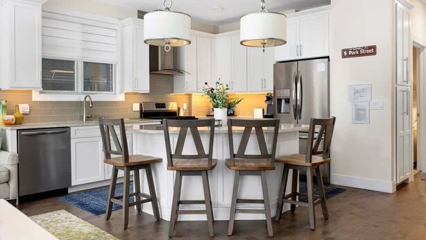 A modern kitchen with white cabinets, a central island with bar stools, stainless steel appliances, and pendant lighting. - Park 201 Downtown in the Heart of Traverse City (Traverse City)