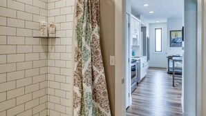 A bathroom with white tiles, a shower curtain with a floral pattern, and a shelf with toiletry bottles.