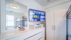 Una habitación de hotel moderna con un espejo grande, un televisor de pantalla plana montado sobre un tocador blanco y un armario con puerta espejada.