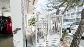 Un espacio al aire libre techado con una terraza de madera, una escalera blanca y una reja metálica.