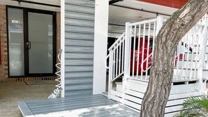 Un espacio al aire libre cubierto con una terraza de madera, barandilla metálica y un árbol.