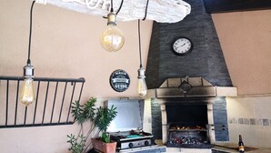 A rustic kitchen with a stone fireplace, hanging light fixtures, and a clock on the wall.