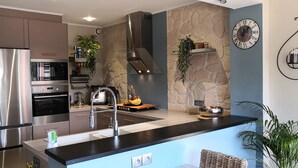 A modern kitchen with stainless steel appliances, a stone accent wall, and a minimalist design.