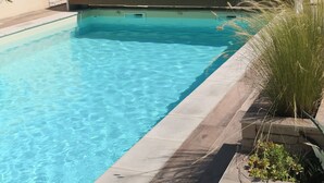 A swimming pool with clear blue water, surrounded by stone tiles and a wooden deck.