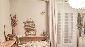 A neatly arranged bedroom with a bed, a bedside table, a shelf with books, and a window with curtains.