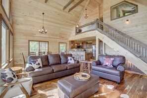 Cozy cabin interior with a high-ceilinged living area, comfortable seating, and a wooden staircase leading to additional living space.