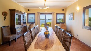 A dining area with a wooden table, wicker chairs, a cabinet, and a view of the sea. - Private waterfront villa with pool and two private beaches (geni)