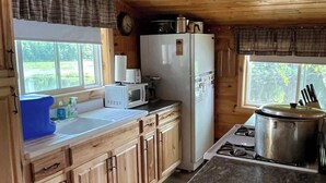 Une cuisine rustique, située dans une cabane en bois, équipée d’un réfrigérateur, d’un four à micro-ondes, d’un évier et d’une cuisinière.