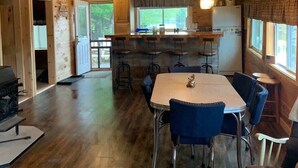 L’intérieur d’un chalet en bois comprend une table à manger, des chaises, un coin cuisine et une cheminée.