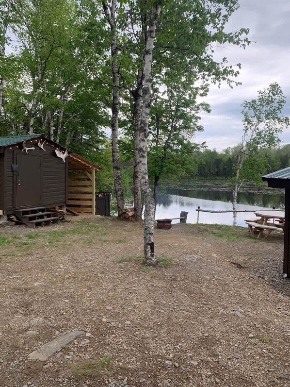 A rustic cabin with a dock extending into a lake, surrounded by birch trees and a picnic table. - Birch Haven: A Pure Off-Grid Maine Escape (North Penobscot)