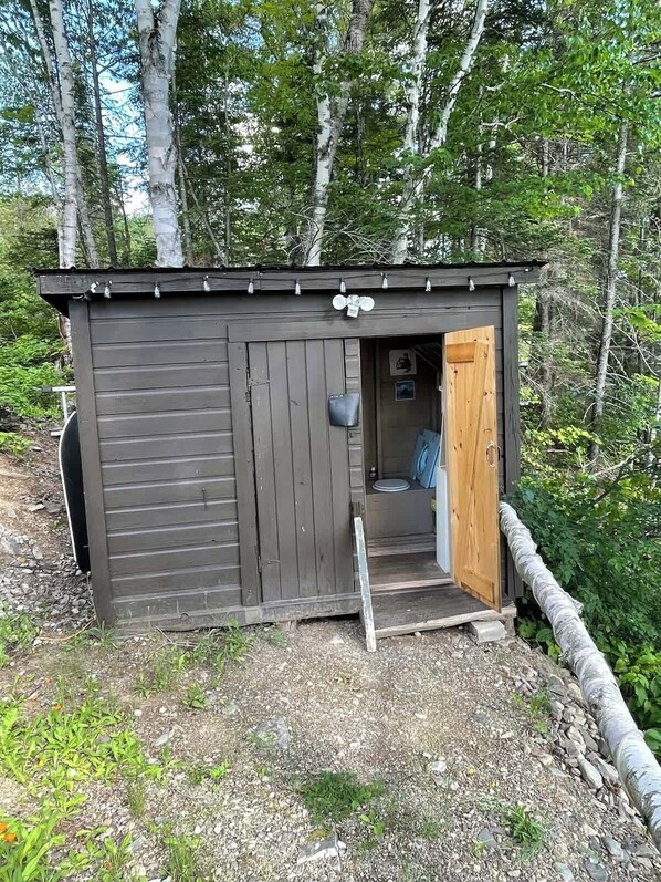 A small wooden shed with a door open, revealing a blue interior. - Birch Haven: A Pure Off-Grid Maine Escape (North Penobscot)