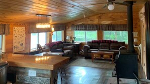 Un intérieur de chalet chaleureux avec un plancher en bois, un espace salon central doté de canapés, un coin cuisine et une cheminée.