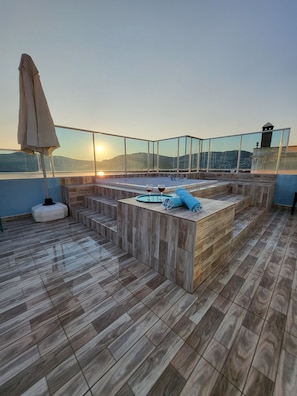 Relax on the rooftop terrace with a seating area and hot tub, surrounded by a glass balustrade offering breathtaking views of the mountains and cityscape.