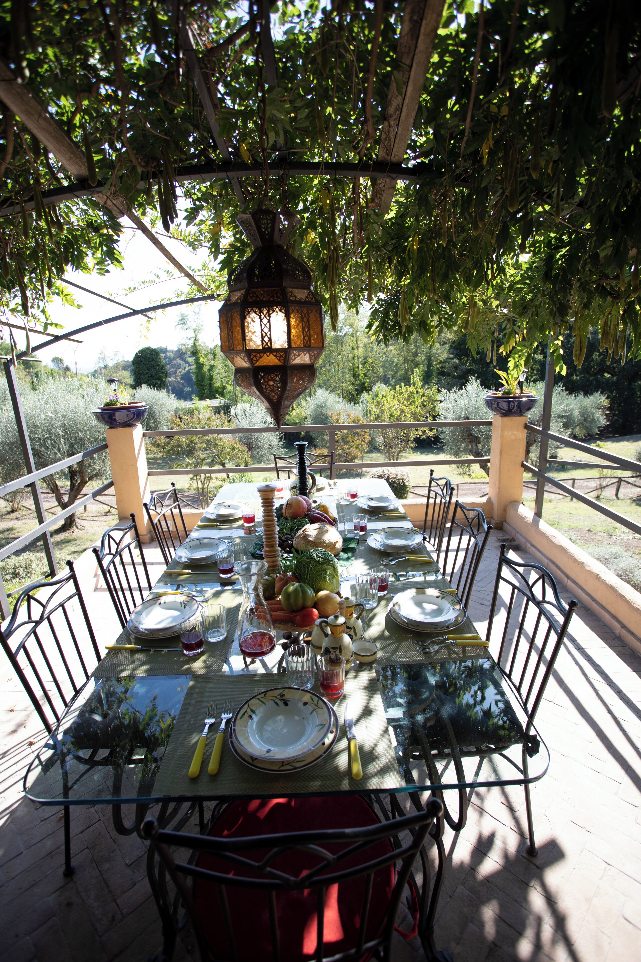 An outdoor dining area with a table set for a meal, surrounded by chairs, and a hanging lantern above.