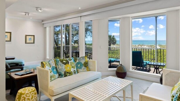 Ein geräumiges Wohnzimmer mit Sofa, Couchtisch und Sesseln, große Fenster mit Meerblick und ein Balkon mit Gartenmöbeln.