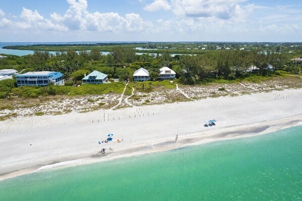 An aerial view of a coastal property with multiple buildings, a sandy beach, and clear turquoise waters.
