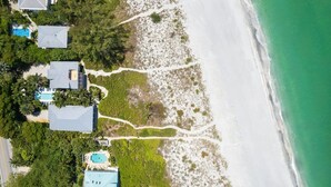 Eine Luftaufnahme einer Küstenimmobilie mit mehreren Gebäuden, einem Strand und einem klaren Weg zum Ufer.
