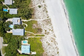 An aerial view of a coastal property with multiple buildings, a beach, and a clear path leading to the shore. - A Saba Wind South- Oceanfront Estate with Pool on Captiva Island! (Captiva)