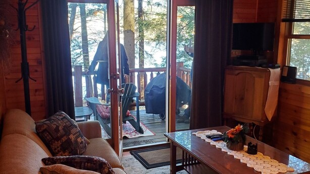 A cozy cabin interior with a wooden sofa, a dining table with a lace tablecloth, and a television.