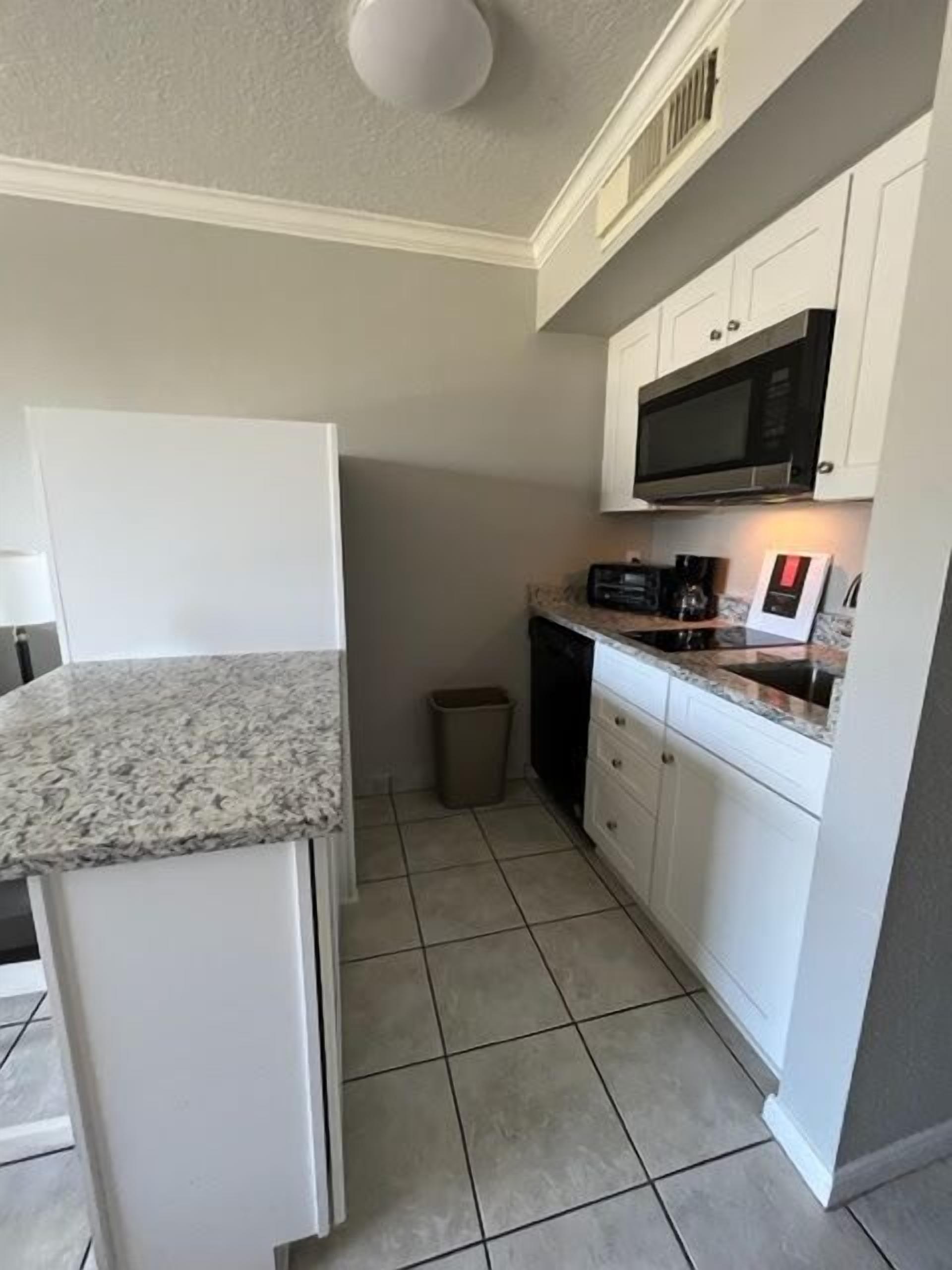A compact kitchen with white cabinets, a granite countertop, a microwave, and a coffee maker.