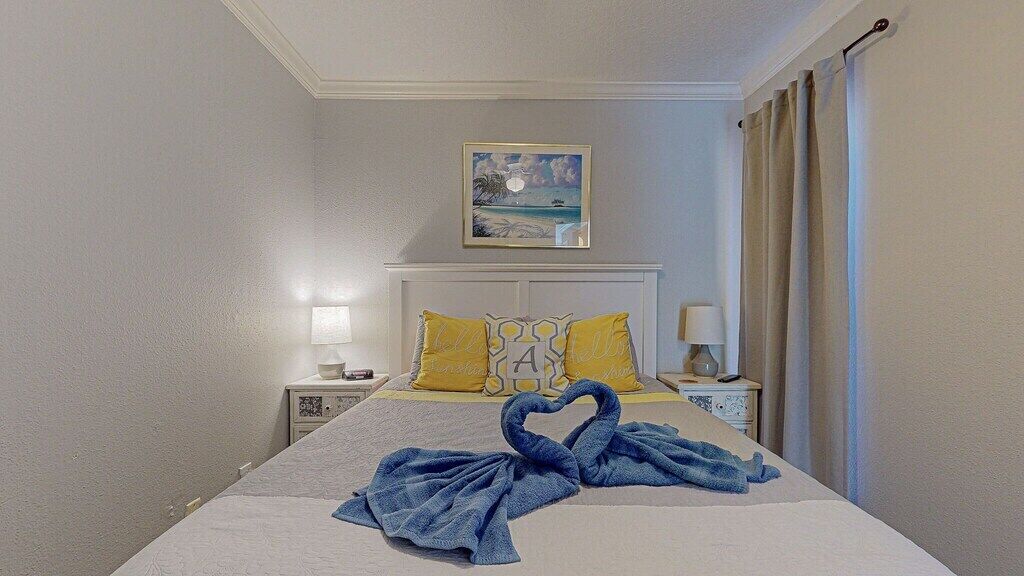 Une chambre d’hôtel avec un lit, deux tables de chevet, un tableau au mur et une fenêtre avec des rideaux.