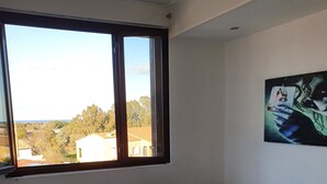 A bedroom with a large window, a bed with white bedding, and a wall with a painting.