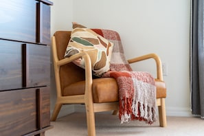 A corner room with a wooden chair, a patterned throw pillow, and a red and white blanket.