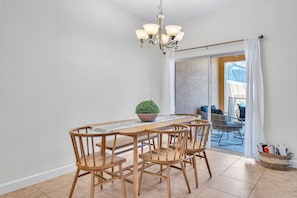 A dining area with a wooden table and chairs, a chandelier, and a view of the outside.