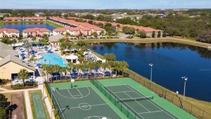Vista aérea de un resort con piscina, canchas de tenis y un lago.
