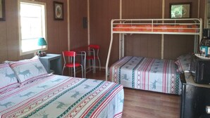 Huoneessa on kaksi sänkyä, kerrossänky, pöytä tuoleineen, lamppu ja jääkaappi.