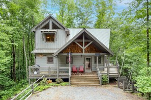 A cabin with a wooden deck, two red Adirondack chairs, and a small porch area.