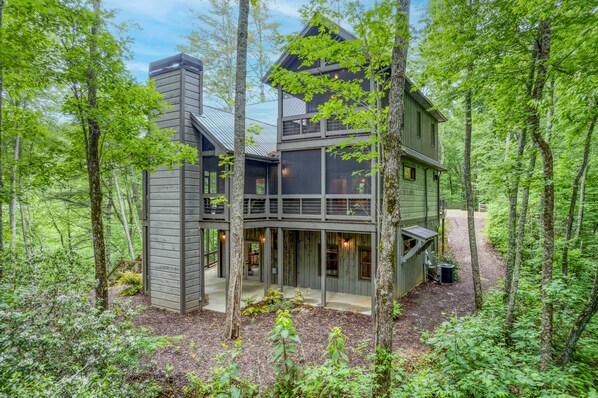 Un chalet moderne à plusieurs niveaux, entouré d’une forêt.