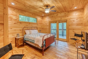 Une chambre dans une cabane en bois, avec un lit, un ventilateur de plafond, une petite table et une chaise.
